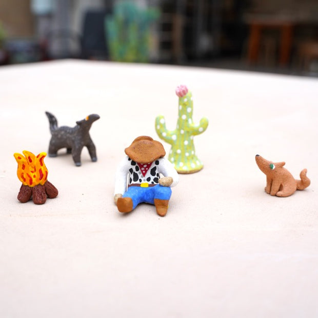 Set of miniature cowboy figurine, cactus, and animals on a white surface