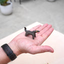 Hand holding a small figurine of an abstract horse on a light surface