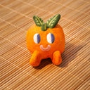 Small sculpture of an orange with 2 green leaves, and a cute cartoon face with purple eyes looking to the side and a simple smile. It lays on its "stomach" with its feet up and head resting in its hands.