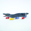 Ceramic sculpture of a blue eel with small, colorful polkadots and an open mouth with tiny teeth. The eel has 5 feet, all wearing sneakers either blue, red or yellow.