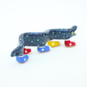 Ceramic sculpture of a blue eel with small, colorful polkadots and an open mouth with tiny teeth. The eel has 5 feet, all wearing sneakers either blue, red or yellow.