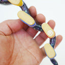 Ceramic sculpture of a blue eel with small, colorful polkadots and an open mouth with tiny teeth. The eel has 5 feet, all wearing sneakers either blue, red or yellow. Underside.