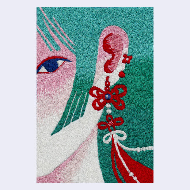Embroidered illustration of the close up of a woman's ear. She has teal hair with straight bangs and wears a long, ornate red tassel earring. Her skin has pinkish tones.