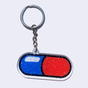 Die cut acrylic keychain with an illustration of a pill, half blue and half red with a cartoon like white shine spot.