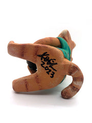 Sculpture of a cartoon style orange tabby cat, sitting with its legs out in front and eyes closed. It holds a pińa colada in its paws and wears a Hawaiian shirt. Viewed from the below, featuring the artist's signature.