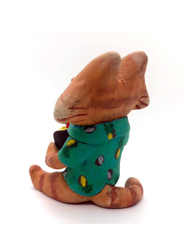 Sculpture of a cartoon style orange tabby cat, sitting with its legs out in front and eyes closed. It holds a pińa colada in its paws and wears a Hawaiian shirt. Viewed from the back.