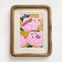Risograph print of 2 brown birds sitting in pink flowers, with yellowish green leaves around them. The print is within a wooden frame with rounded corners and held in place by 2 mats.