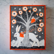 Black ink drawing with orange accent coloring of a large tree with blooming flowers. A woman sits on one of its branches and hangs a star. Below, another woman rides by atop a very large white bunny.