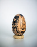 A hand-painted wooden egg with a detailed illustration of a cat holding a candle, with a sun overhead and within a nice border.
