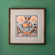 Framed artwork on a green wall. Artwork is a black and orange ink illustration of a cat, curled up underground like a seed - with an orange flower blooming from it. Around the cat are plant characters/creatures with an orange ribbon.