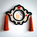 Decorative wall piece with tassels embroidered detailing and with an artwork within it - Illustration of a witch wearing a dress and a hat and holding a wand, conjuring a very large fire, which casts the surroundings into darkness.