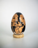A decorative wooden egg with black illustrations of floral and animal illustrations, displayed upright on a small cork-like base against a light gray studio background.