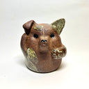 Ceramic sculpture of a cute, brown dog with its paws on its cheek and a rounded bottom without legs. It has green textured spots.