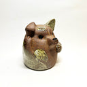 Ceramic sculpture of a cute, brown dog with its paws on its cheek and a rounded bottom without legs. It has green textured spots.