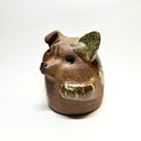 Ceramic sculpture of a cute, brown dog with its paws on its cheek and a rounded bottom without legs. It has green textured spots.