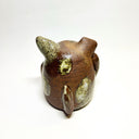 Ceramic sculpture of a cute, brown dog with its paws on its cheek and a rounded bottom without legs. It has green textured spots.