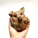 Ceramic sculpture of a cute, brown dog with its paws on its cheek and a rounded bottom without legs. It has green textured spots.