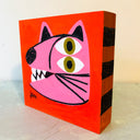 Painting on wooden panel of a folk art style pink cat head with 2 eyes, stacked atop of one another. It has sharp white teeth and a subtle smile.