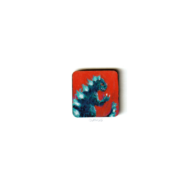 Small square wooden panel with an illustration of a blue Godzilla with glowing back scales. 