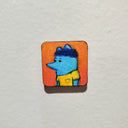 Tiny illustration on a wooden panel of a blue mouse character.