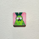Illustration of a green pickle with pink background on tiny panel.