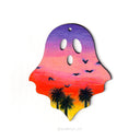 Ghost shaped wood panel with an illustration of a colorful sunset on it, with silhouetted palm trees and birds flying.