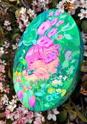 Painting on oval shaped wooden panel of a girl with pink hair and an apathetic expression sitting in very lush greenery, with blue, purple pink and white flowers in front of her and more greenery behind her.