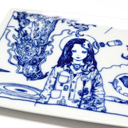 Rectangular white porcelain plate with dark blue line art illustrations of 2 scenes, divided like a comic panel. Left scene depicts a person with long hair and robotics coming out of their head. A dragon flies down behind them. Detail photo.