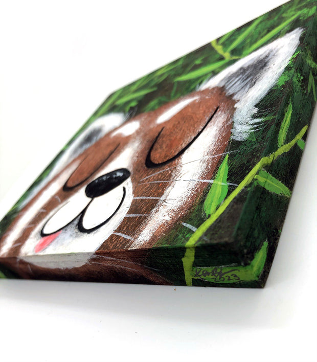 Illustrative style painting of a cute, red panda with large closed eyes and a smiling tongue out expression. Only its head is visible but it takes up most of the surface, with bamboo behind it.