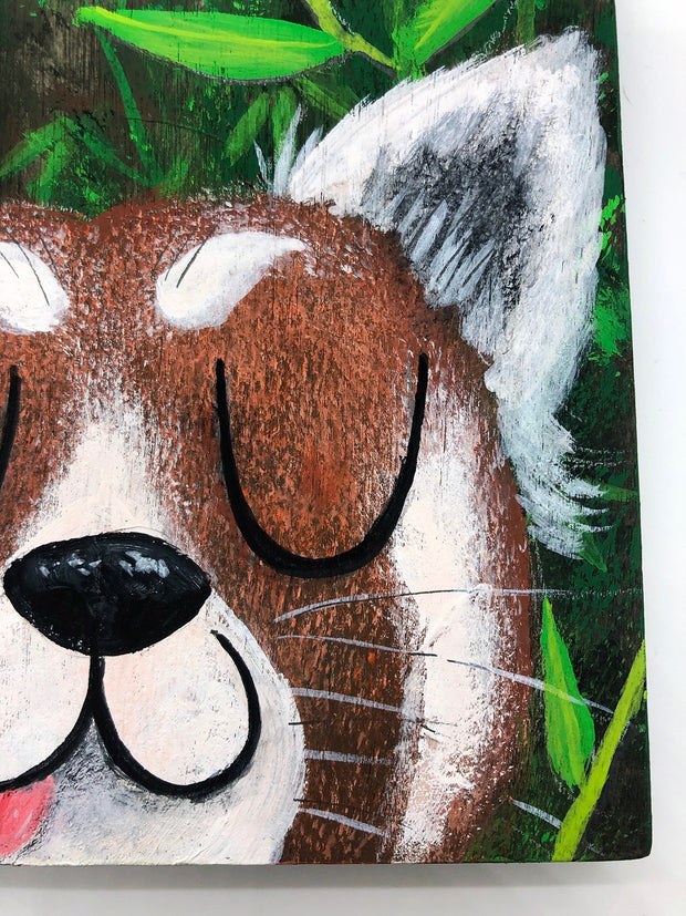 Illustrative style painting of a cute, red panda with large closed eyes and a smiling tongue out expression. Only its head is visible but it takes up most of the surface, with bamboo behind it.