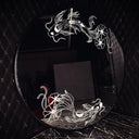 A round black mirror featuring white etched illustrations of 2 koi fish with lily pads, one atop and one at the bottom, set against a dark quilted wall and dark marble surface.