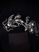 A round black mirror featuring white etched illustrations of 2 koi fish with lily pads, one atop and one at the bottom, set against a dark quilted wall and dark marble surface.