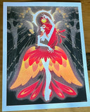 A brightly colored risograph print of a stylized dancer or fairy figure with large red, orange, and yellow wing-like forms on a dark background, photographed flat on a wooden surface.