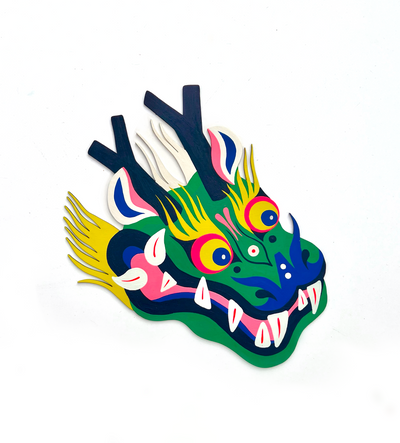 Die cut, brightly painted wooden sculpture of a folklore style dragon head, with deer like antlers atop its head and sharp teeth curving out of its mouth. Its head is green with blue and pink accenting, with wild yellow eyebrows and beard.