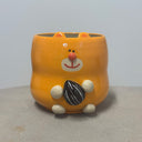 Ceramic cup modeled like an orange cartoon hamster, sitting and holding a sunflower seed. 