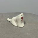 Ceramic figurine of a cartoon style white cat with a droopy, simplistically cute face with a large round red nose.