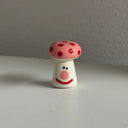 Tiny ceramic sculpture of a pink mushroom with a cartoon smile.