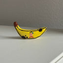 Tiny ceramic sculpture of a rotten banana with a sad cartoon face.