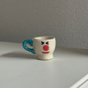Tiny ceramic sculpture of a teacup with a cartoon face.