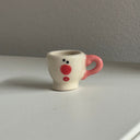 Tiny ceramic sculpture of a teacup with a pink handle.