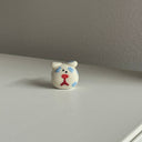 Tiny ceramic sculpture of a cartoon dog's head, white with blue spots and a cartoon frown.