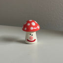 Tiny ceramic sculpture of a red mushroom with spots and a cute cartoon smile.
