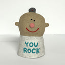 Ceramic sculpture of a boy's top half, without arms. He wears a white sweater that says "you rock" and has a tiny pet rock atop his head.