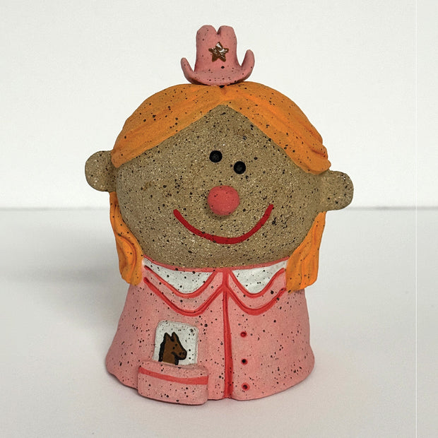 Ceramic sculpture of a girl's top half, without arms. She wears a pink cowgirl style button up and a tiny pink cowgirl hat with a star.