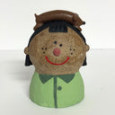 Ceramic sculpture of a girl's top half, without arms. She wears a green button up and has a brown dog atop her head, laying on its long body.