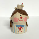 Ceramic sculpture of a girl's top half, without arms. She wears a striped shirt, smiles and has a chicken with an egg atop her head.