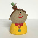 Ceramic sculpture of a girl's top half, without arms. She wears a yellow shirt with colorful buttons. Atop her head is a small snail with a green shell.