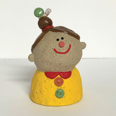 Ceramic sculpture of a girl's top half, without arms. She wears a yellow shirt with colorful buttons. Atop her head is a small snail with a green shell.