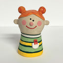 Ceramic sculpture of a girl's top half, without arms. She wears a striped sweater with a small red dog coming out of her lapel pocket. She has orange hair, done up in 2 buns.