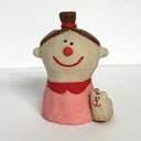 Ceramic sculpture of a girl's top half, without arms. She wears a pink shirt with a red collar and has her short brown hair in a high ponytail. Next to her side is a small fluffy dog.